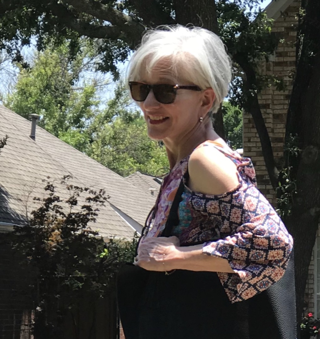 A woman with white hair wearing sunglasses and a floral top.