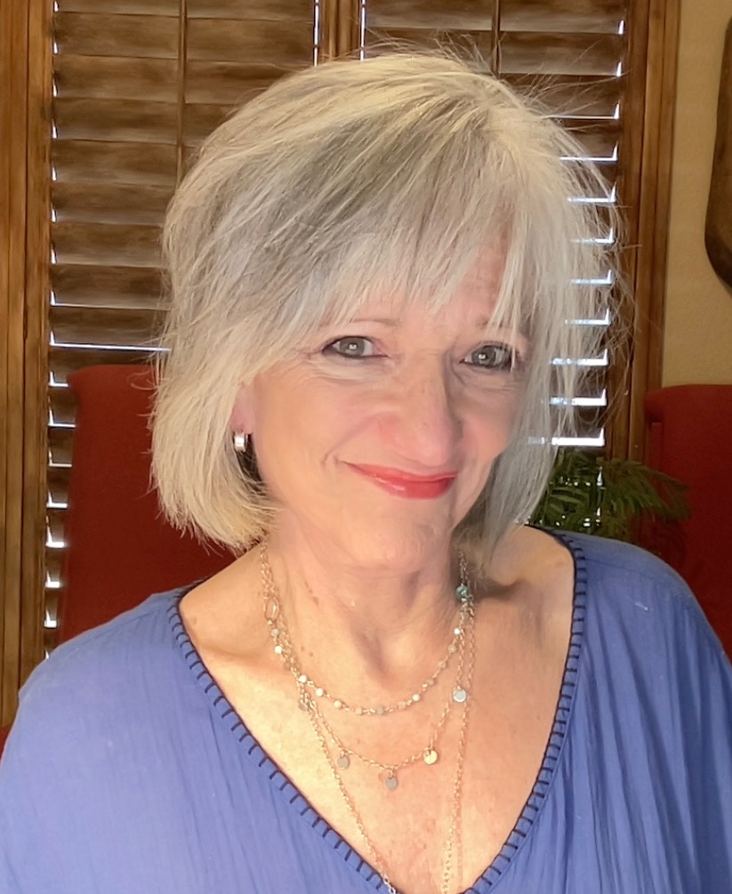 A woman with white hair wearing blue shirt and necklace.